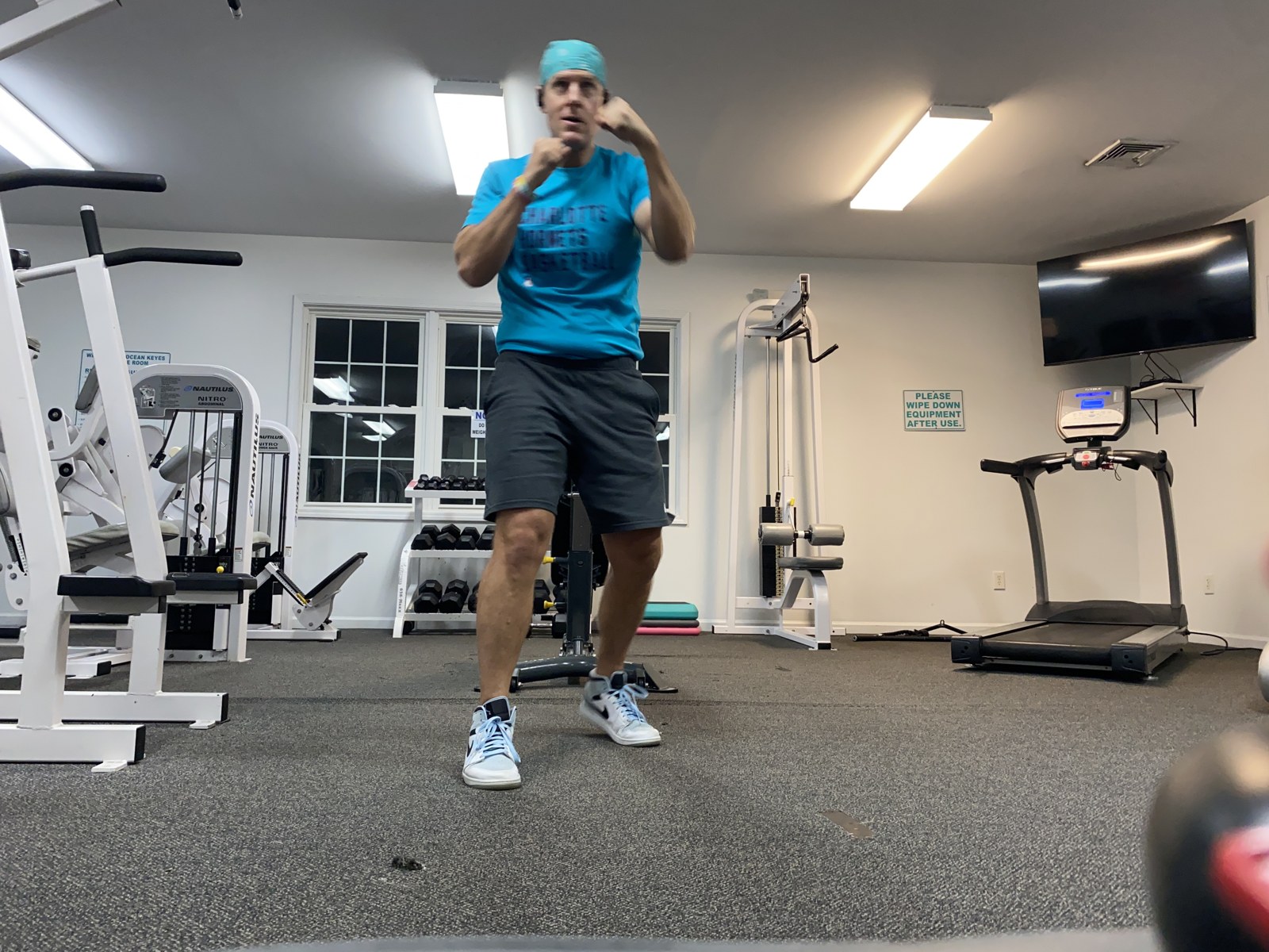Chad facing the camera with both fists up in a boxing guard, condo gym, early morning.